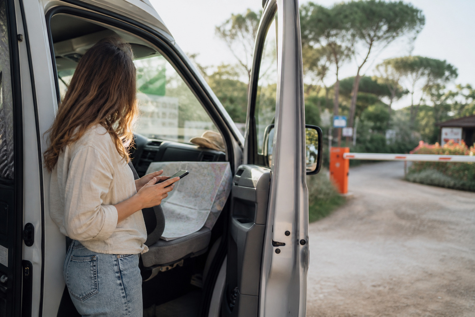 Voyageuse consultant les disponibilites des campings sur son telephone devant son van, a l entree d un camping